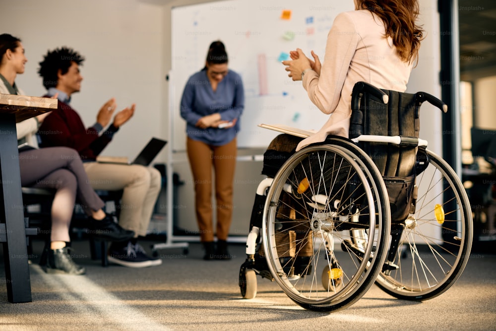 휠체어를 탄 사업가와 회의실에서 프레젠테이션을 하는 동안 박수를 치는 동료들의 뒷모습.