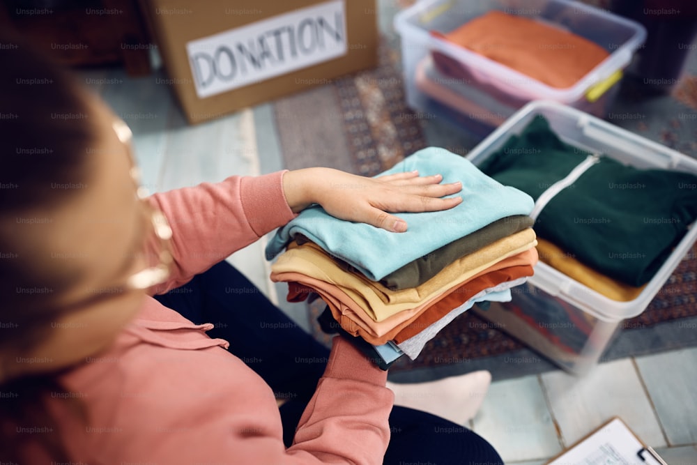 寄付された衣類を箱に整理する女性ボランティアのクローズアップ。