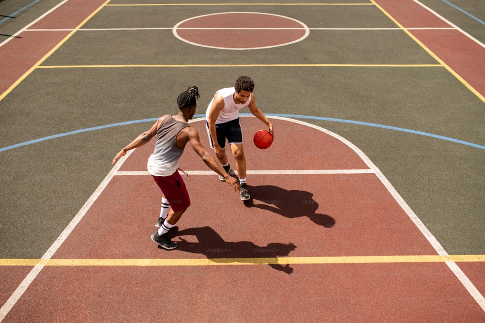 Junger Basketballspieler, der versucht, den Ball vor dem Rivalen zu verteidigen, während er ihn während des Spiels auf dem Außenplatz trägt