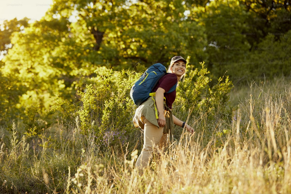 Vista de baixo ângulo da mulher feliz com caminhada de mochila enquanto passa um dia na natureza.