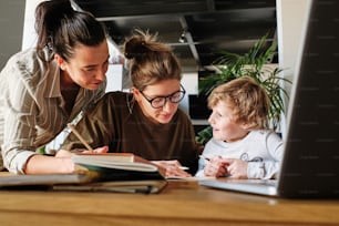 Young homosexual mothers teaching their little son together at table with books