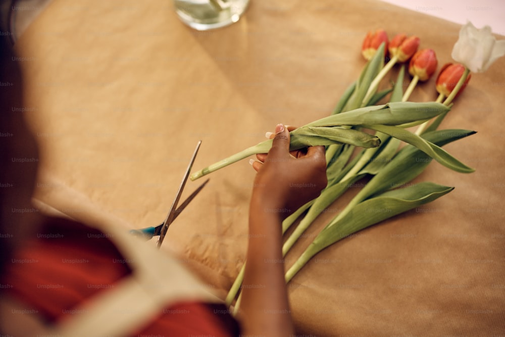 Primer plano de una mujer cortando tulipanes mientras hace un ramo en una floristería.
