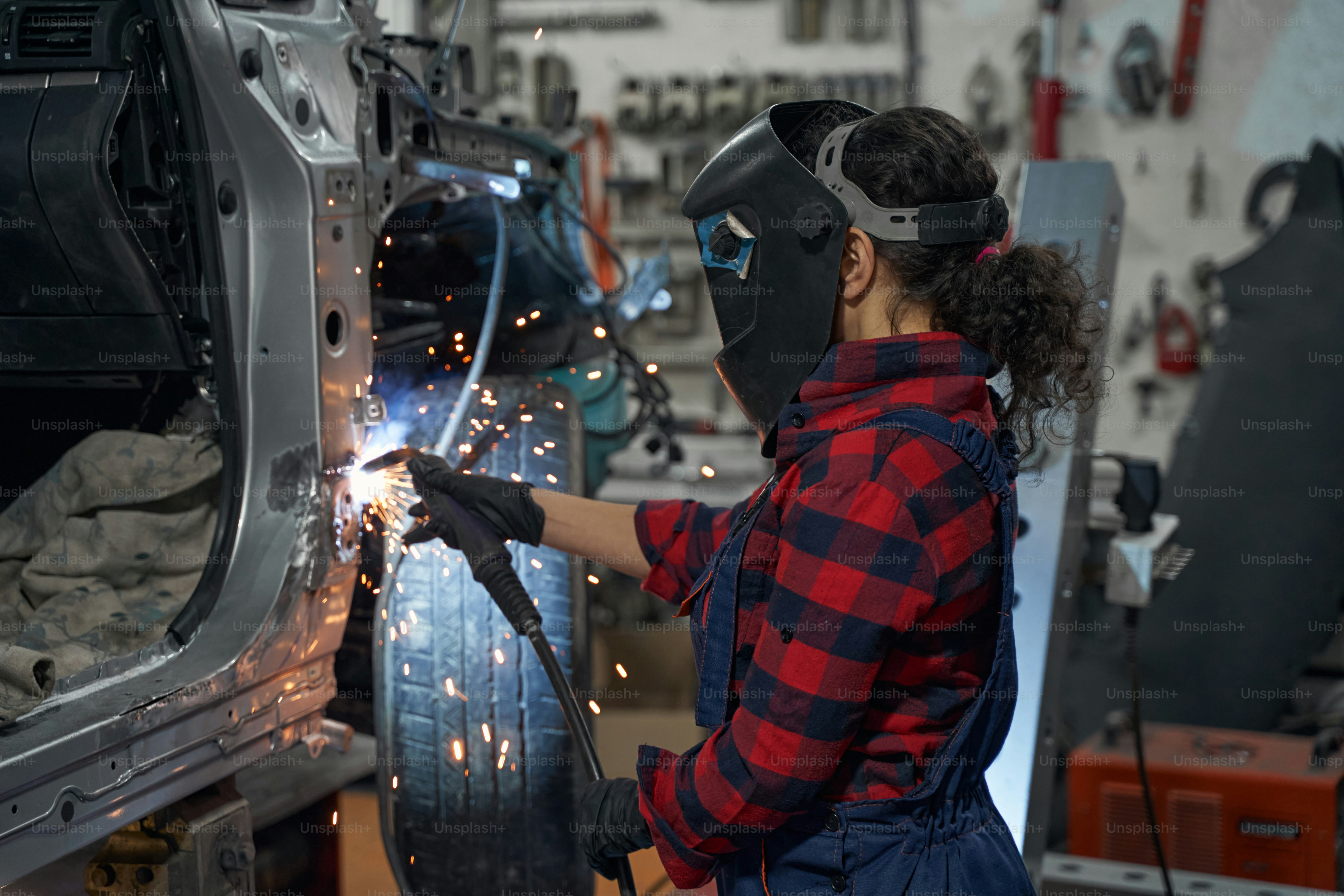 Young mechanic wearing helmet while welding metal, working in garage ...