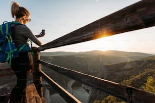 Joven excursionista tomando foto con un teléfono inteligente desde el mirador del cañón.