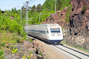 Trem elétrico de alta velocidade corre através de um cânion em uma área rochosa montanhosa