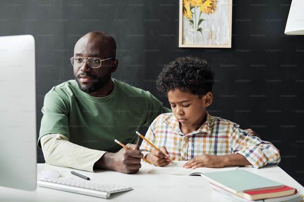 African father helping his son in study while they sitting at the table and studying at home