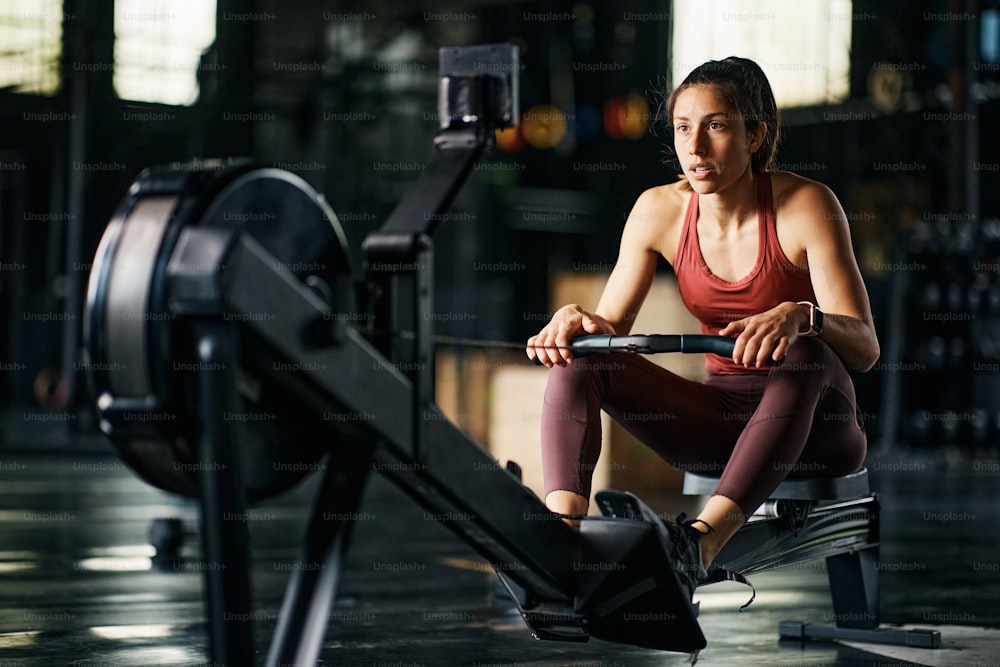 Determined athletic woman watching timer on rowing machine while having cross training in a gym.