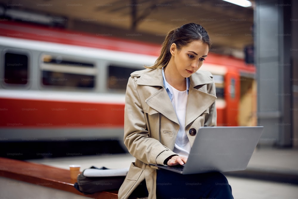 Mujer joven usando una computadora portátil mientras espera el viaje en el metro.