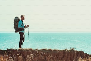 The traveler with backpack standing on the mountain top above the sea