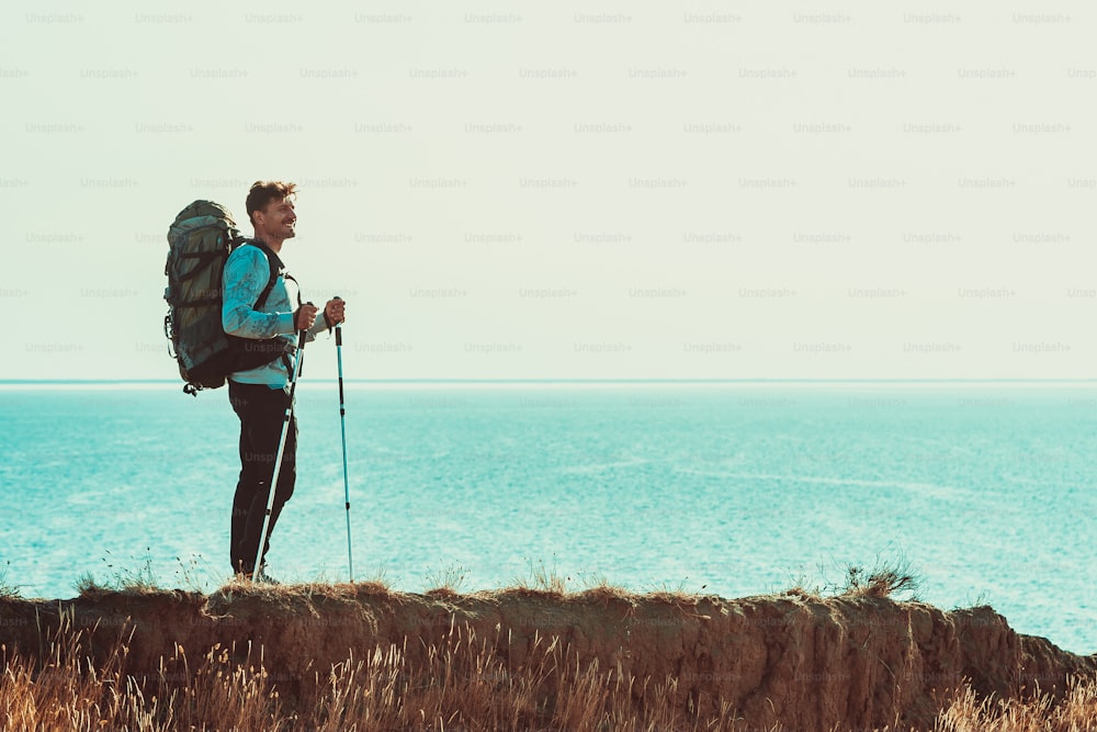 The traveler with backpack standing on the mountain top above the sea