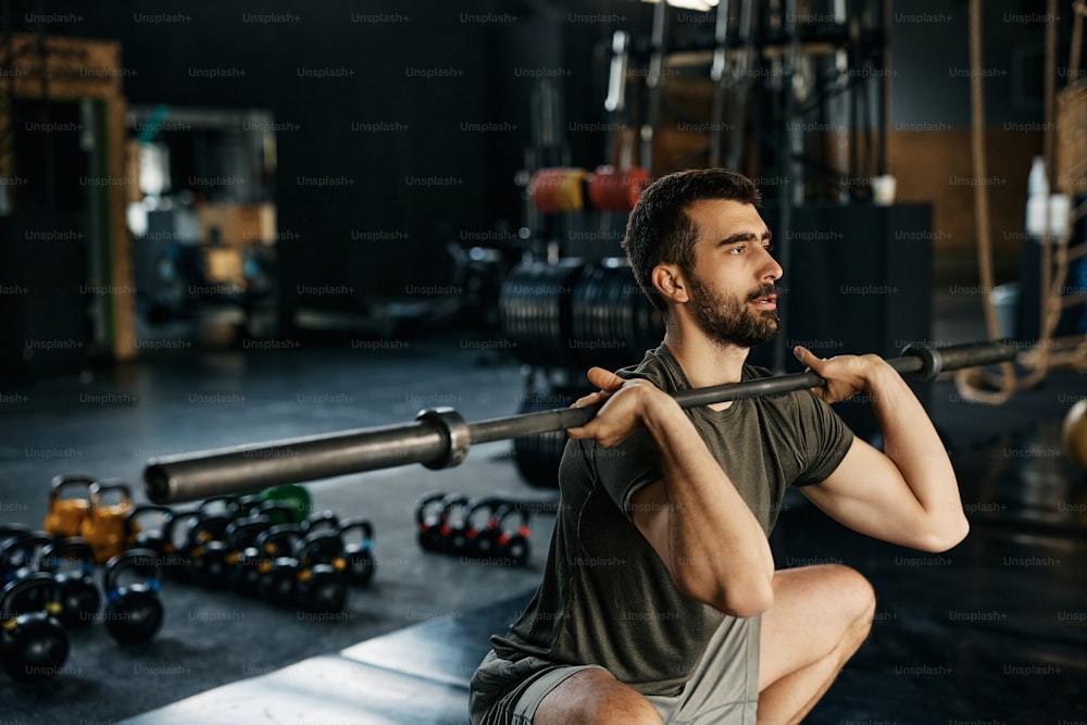 Atleta masculino usando barbo mientras hace sentadillas durante el entrenamiento deportivo en un gimnasio.