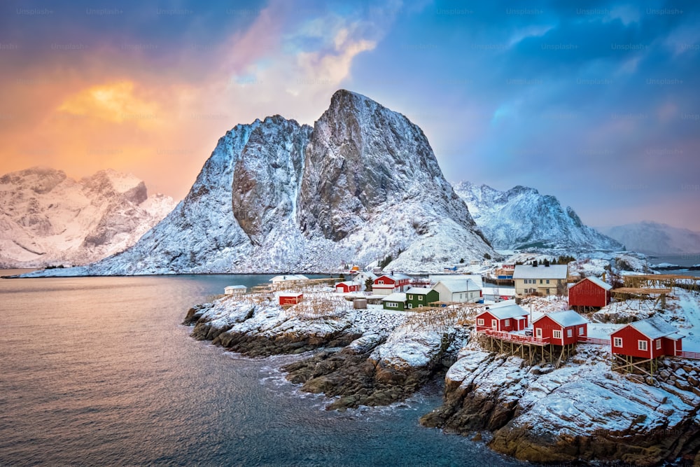 ノルウェーのロフォーテン諸島にある有名な観光名所ハムノイ漁村で、赤いロルブの家があります。日の出に降る冬の雪と
