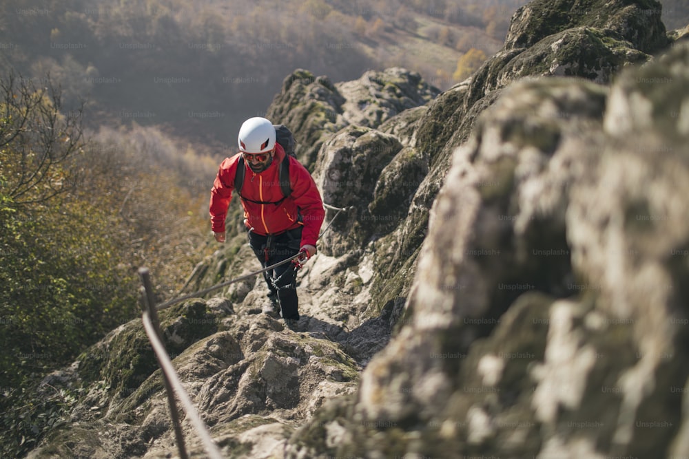 Homem totalmente equipado escalando montanha ao longo de uma via ferrata.