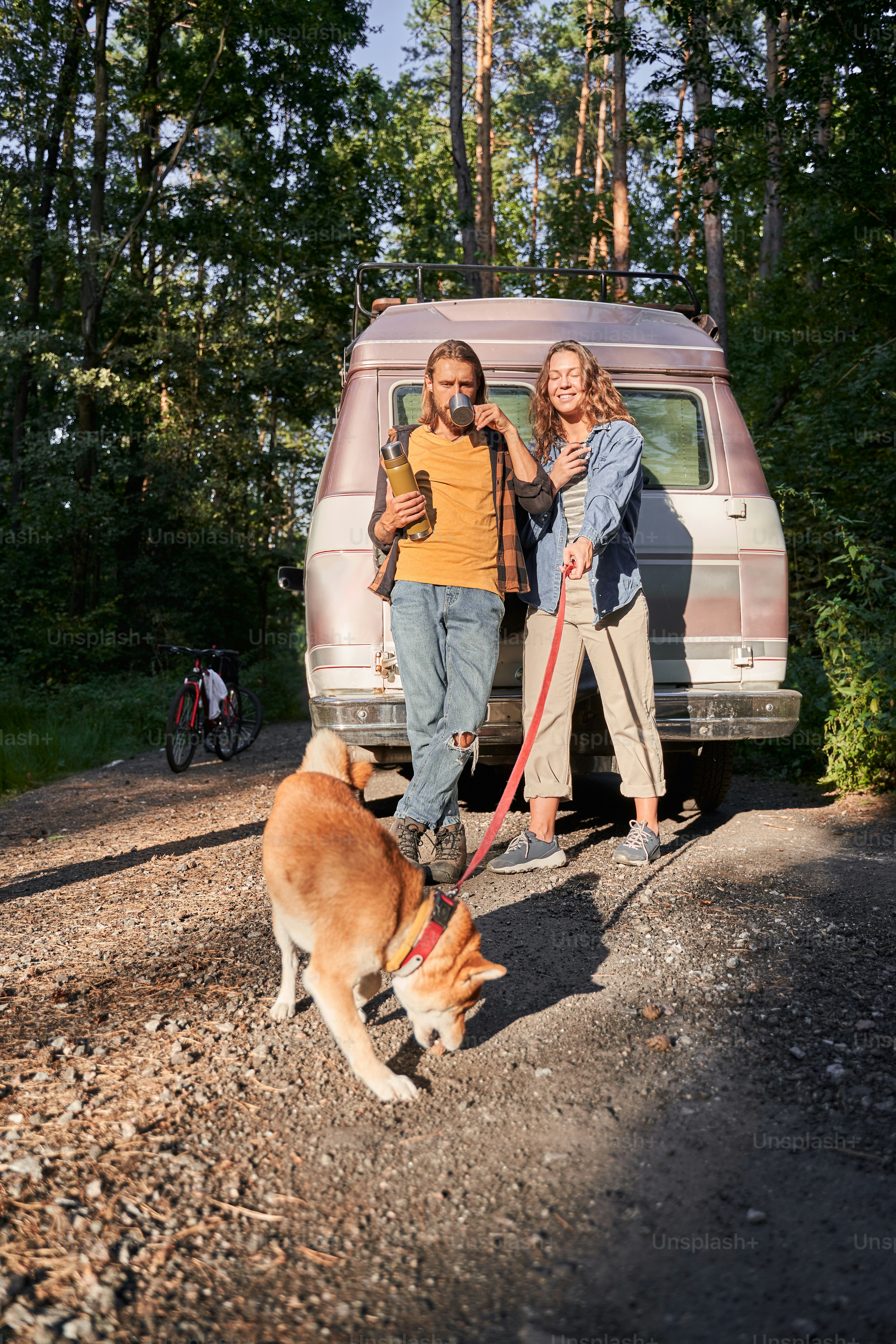 Young loved couple of tourists have a date in the forest. Attractive young woman and handsome man are spending time together on nature. Lovers and their dog around the trees