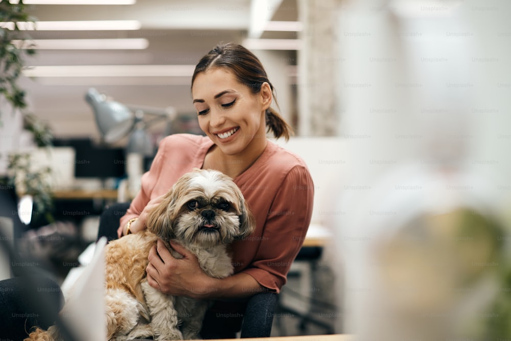 Empresária feliz desfrutando com seu cão enquanto trabalha no escritório. Espaço de cópia.