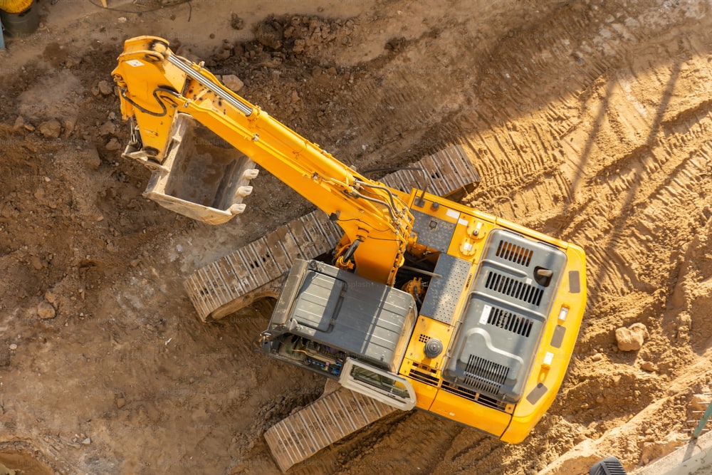 Excavator on the ground of a construction site with a raised bucket, top aerial view