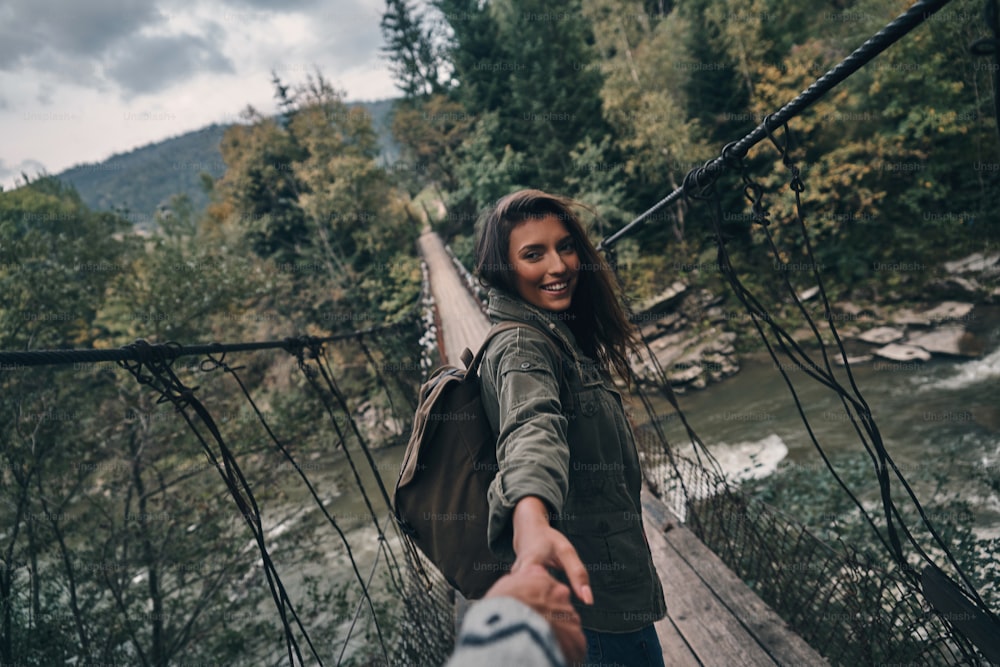 Schöne junge lächelnde Frau, die Händchen mit ihrem Freund hält, während sie auf der Hängebrücke geht