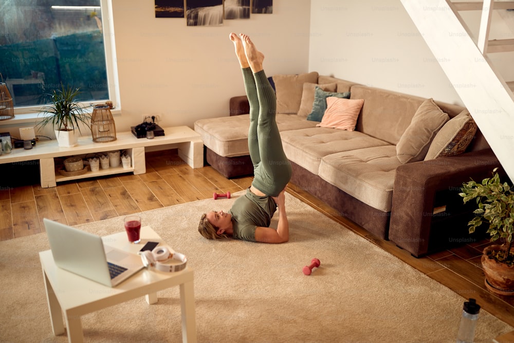 High angle view of athletic woman practicing Yoga in supported shoulderstand pose in the living room.