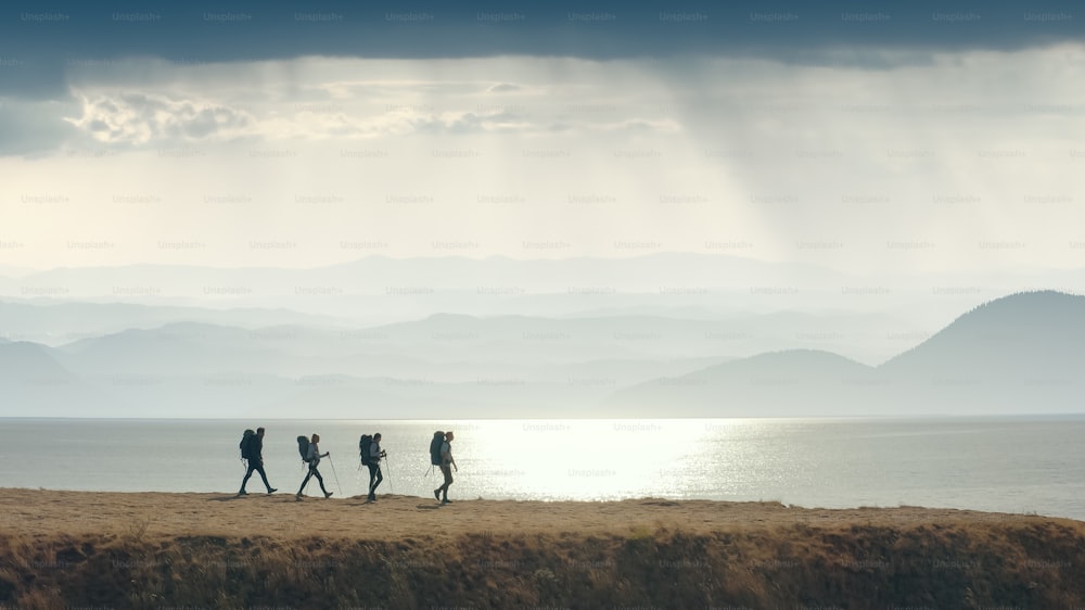 The group of four people walking to the mountain edge near the sea