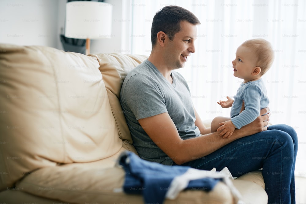 Young smiling father enjoying while talking to his baby son at home.