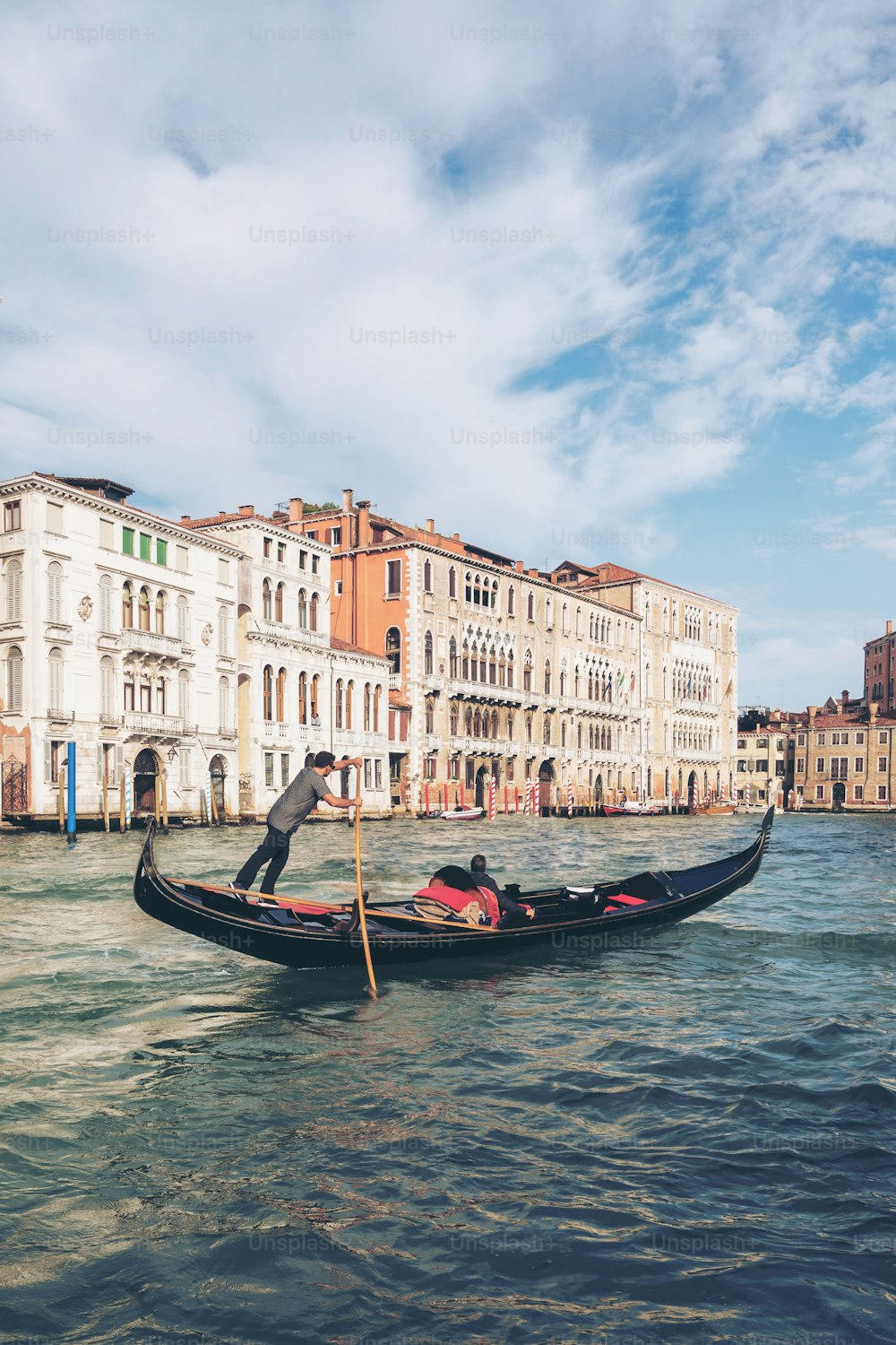 베네치아 곤돌리에가 이탈리아 베니스의 대운하를 통과하는 곤돌라를 펀팅하고 있다. 곤돌라는 바닥이 평평한 전통적인 베네치아 노 젓는 보트입니다. 이탈리아 베니스의 독특한 교통 수단입니다.