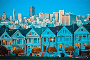 Famous Painted Ladies of San Francisco, California sit glowing amid the backdrop of a sunset and skyscrapers.