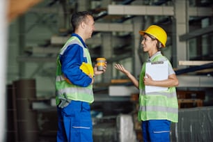 Trabalhador feliz se comunicando com a colega enquanto bebe café em uma pausa no armazém.