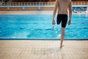 Back view of athletic man with a leg disability standing by the swimming pool. Copy space.