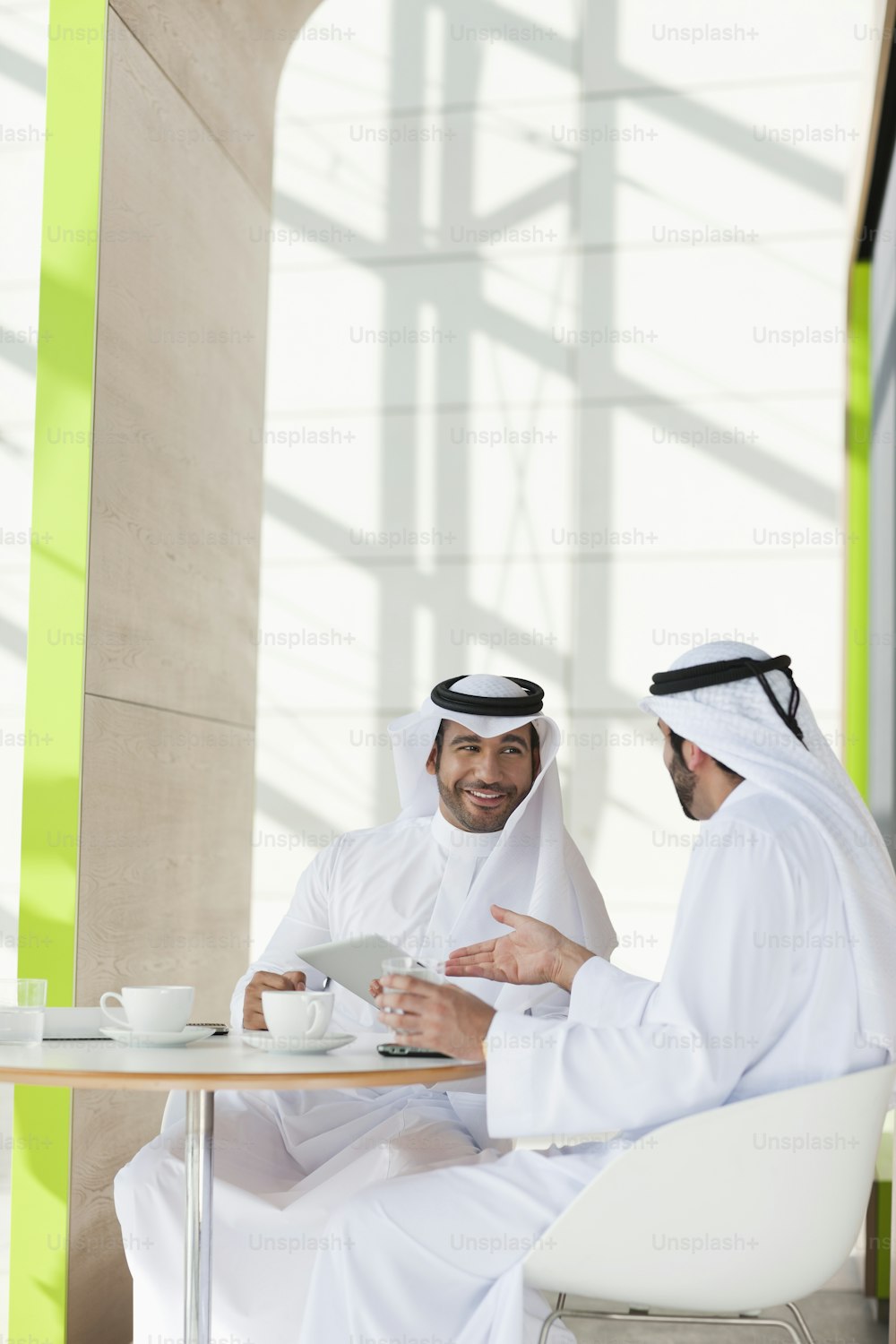 two men sitting at a table with a tablet