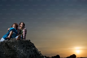um casal de pessoas sentadas em cima de uma rocha