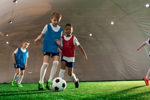 Young football players of various teams trying to kick the ball during game