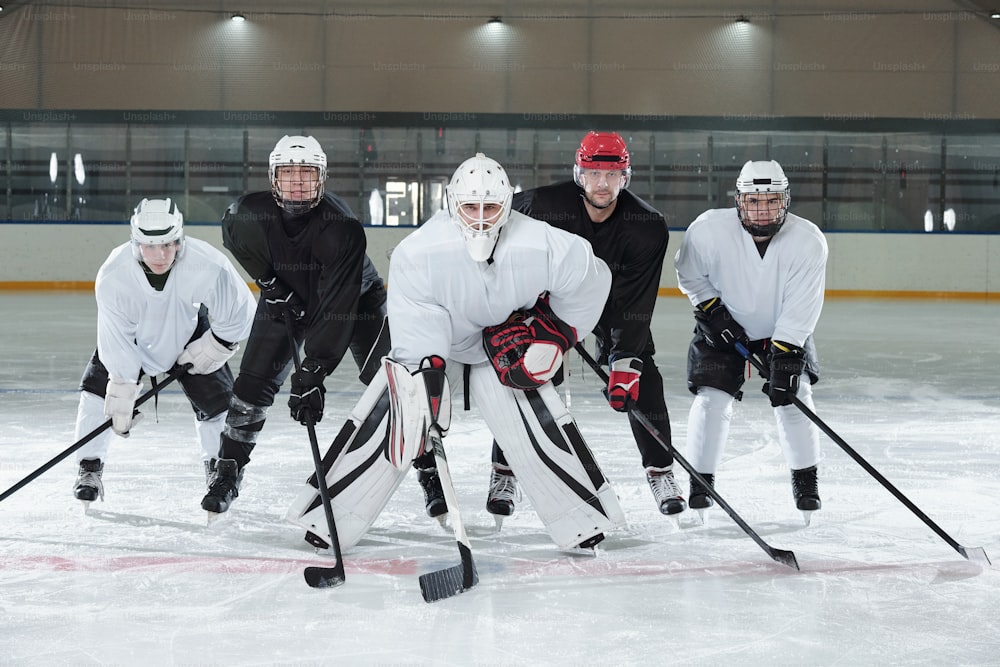 Professional hockey players in gloves, skates and helmets bending forwards while standing on ice rink during training before play at stadium