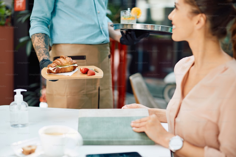 Primo piano del cameriere che serve un panino con croissant a una donna in un caffè.
