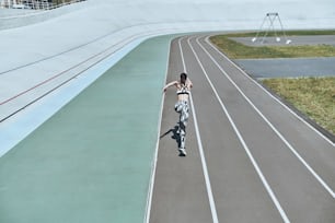 Top rear view of young woman in sports clothing running while exercising outdoors