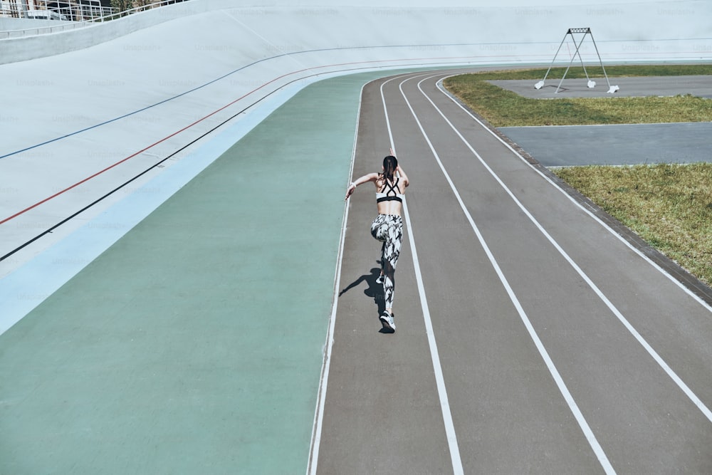 Top rear view of young woman in sports clothing running while exercising outdoors