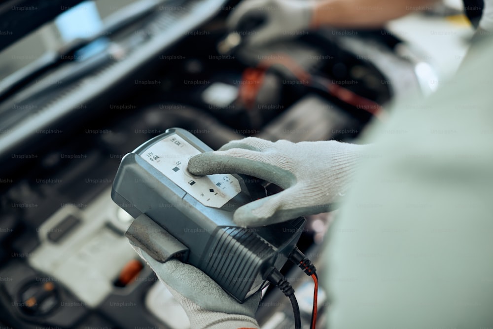Primo piano dell'uomo della riparazione auto che utilizza lo strumento di lavoro diagnostico durante il controllo della batteria dell'auto in un'officina.