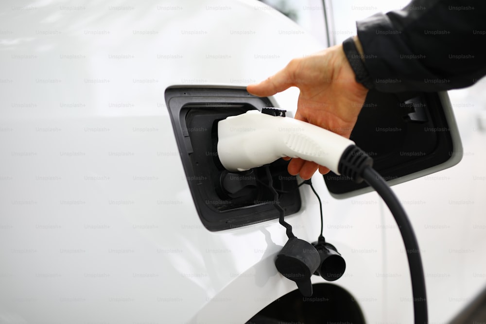 Male hand holds inserts plug for charging into car. Electric cars and charging stations concept