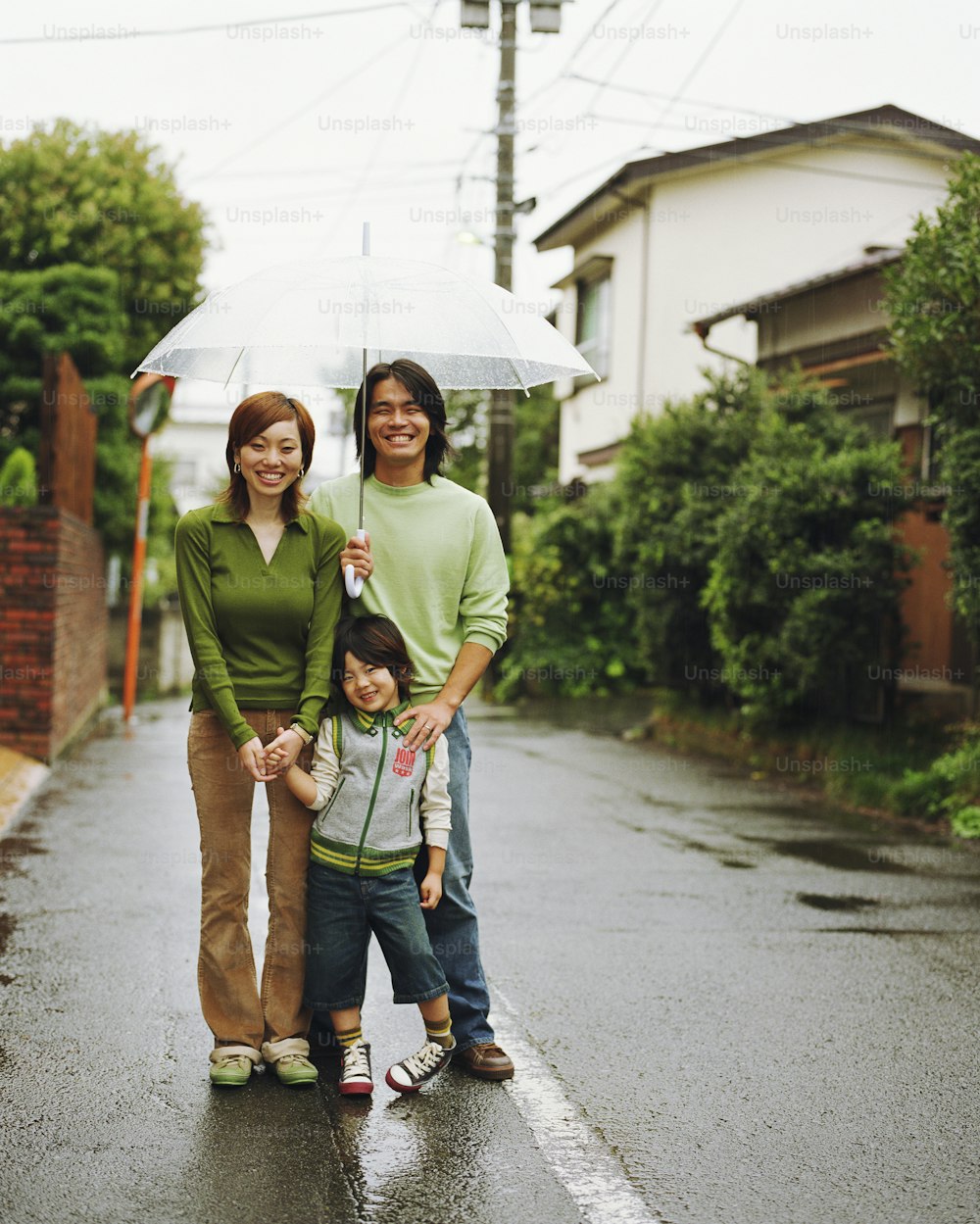 Parents and son (4-6) standing under umbrella, smiling, portrait