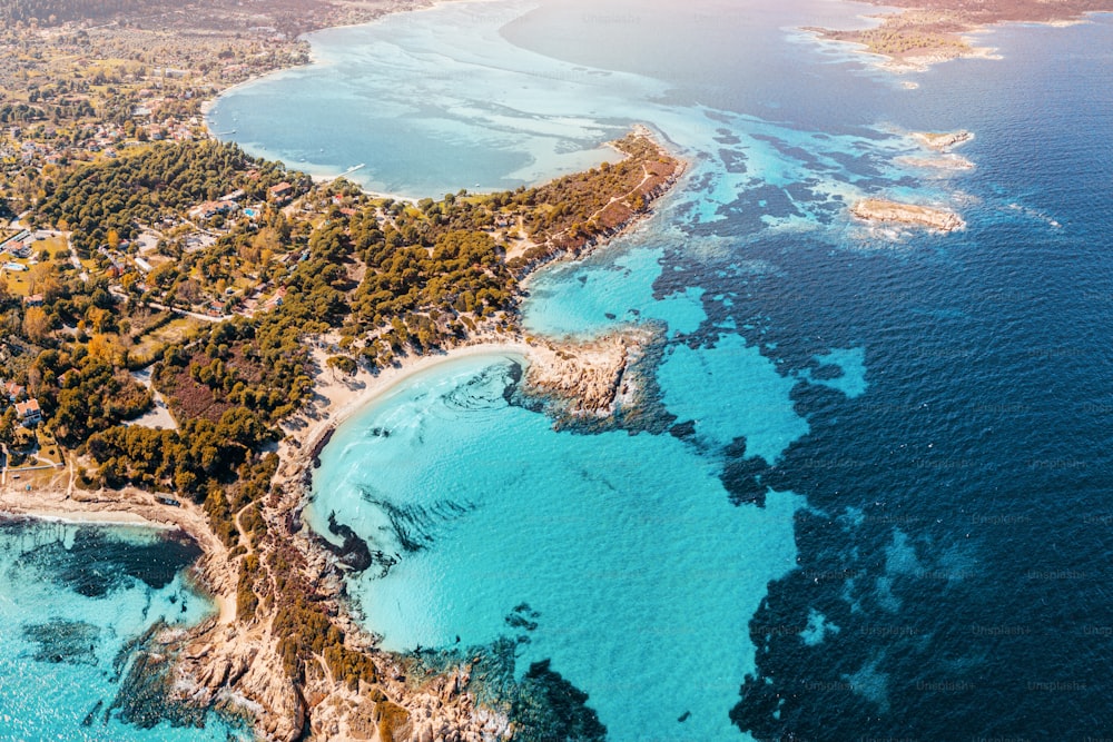 Vista aérea de la paradisíaca orilla del mar con varios tonos de agua turquesa. Arrecifes de coral en profundidad y playas de arena solitarias en el pueblo turístico de Vourvourou en Grecia