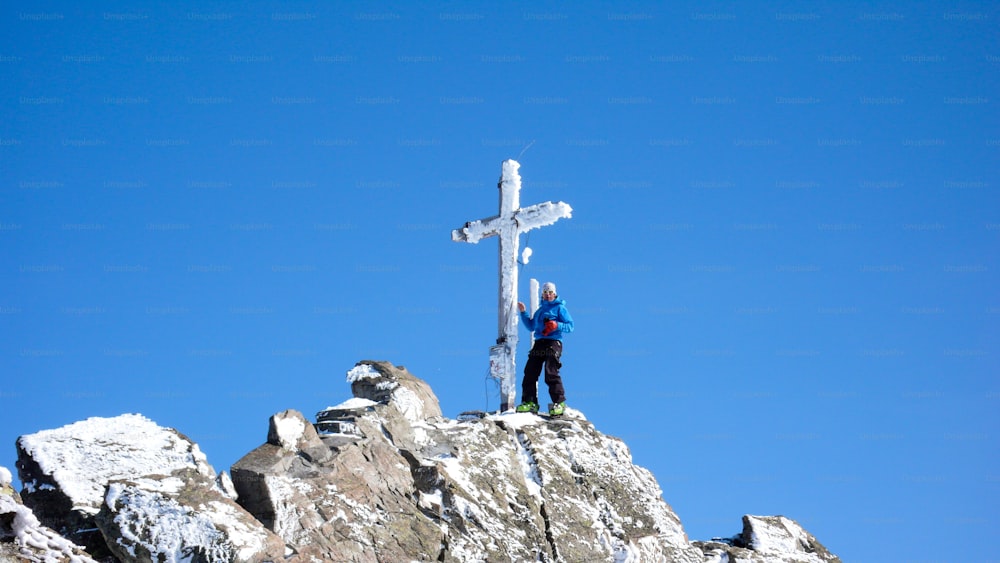 male backcountry skier at the summit cross of a high alpine peak on a beautiful winter day in the Swiss Alps