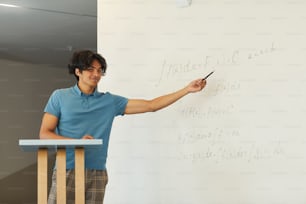 Content confident mixed race student boy pointing at whiteboard while explaining math solution at university class