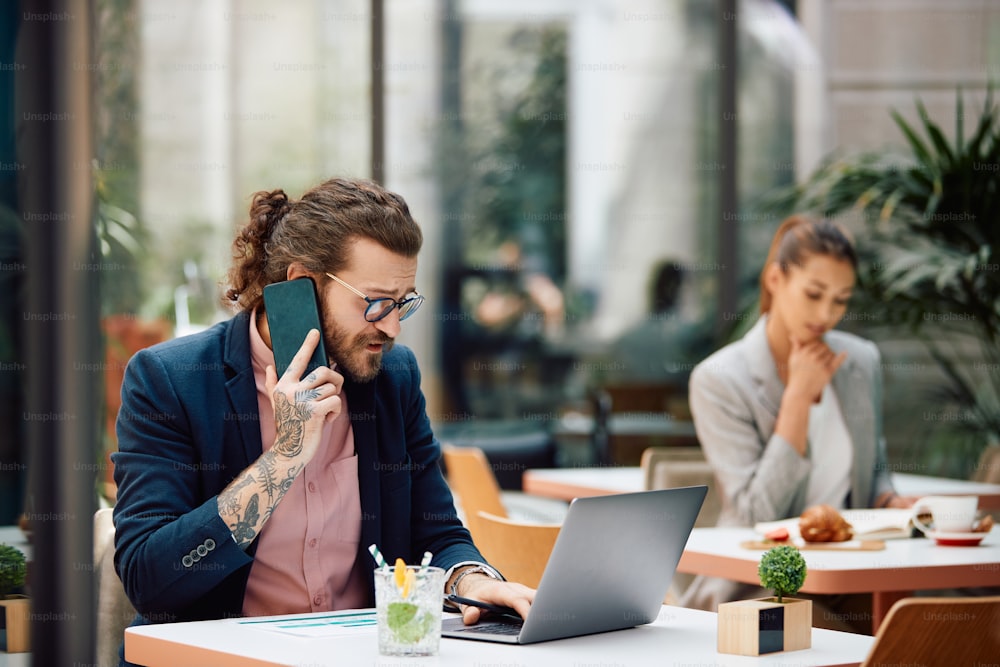 Vielbeschäftigter Unternehmer mit Laptop, während er über Mobiltelefon in einem Café kommuniziert.