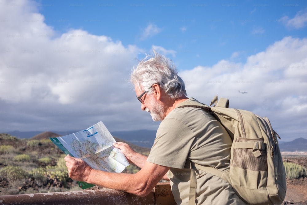 Sorrindo relaxado homem barbudo sênior em excursão ao ar livre consultando seu mapa usando mochila. Aposentado ativo de cabelos brancos desfrutando de caminhadas e estilo de vida saudável
