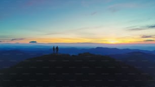 El hombre y la mujer de pie en la montaña en el fondo de la puesta del sol
