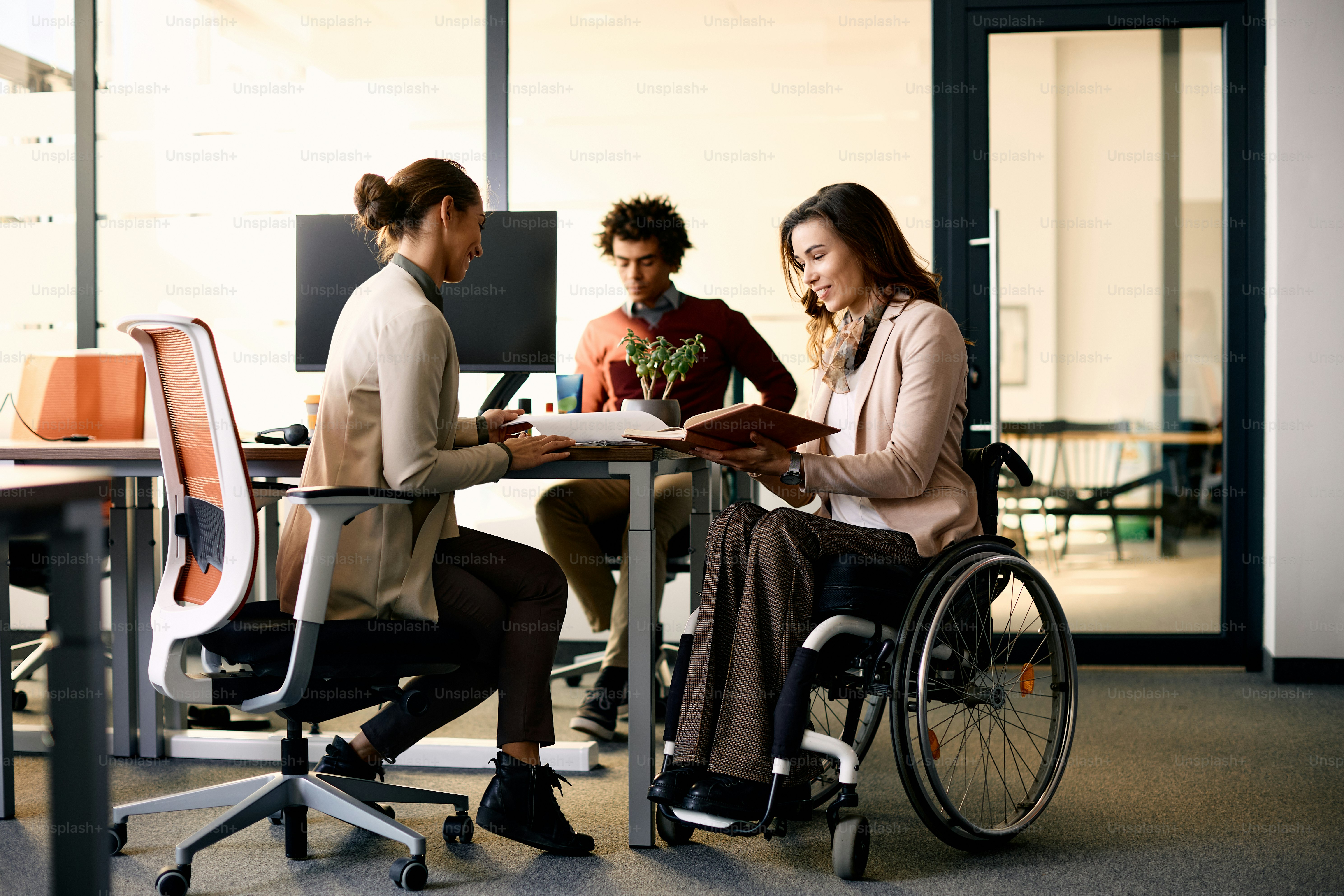 Pengusaha penyandang disabilitas yang bahagia dan rekan wanitanya bekerja sama saat mengerjakan dokumen di kantor.