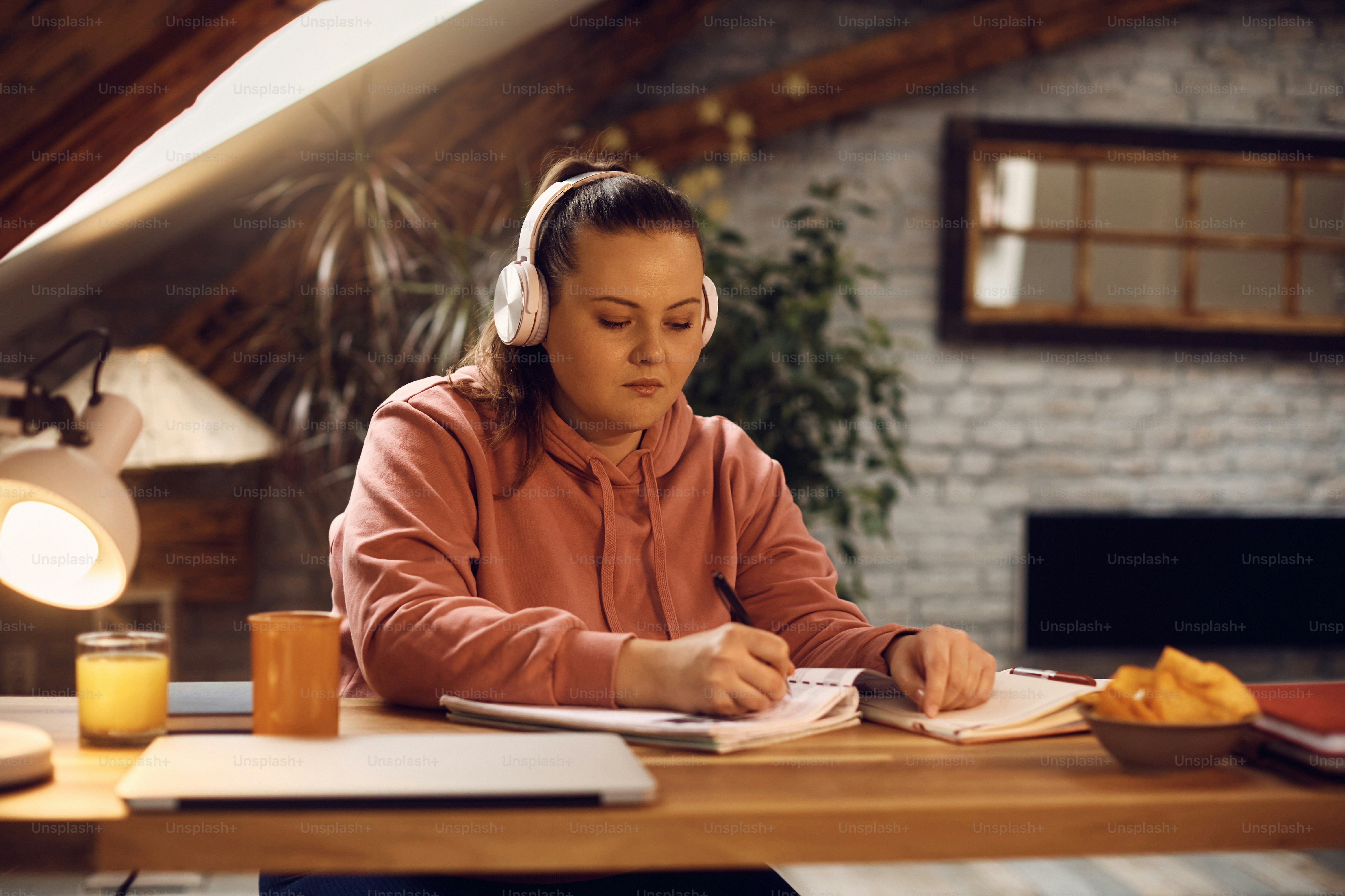 Studentin, die Notizen macht und Musik über Kopfhörer hört, während sie zu Hause lernt.