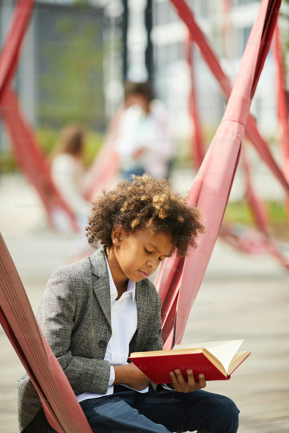 Un escolar africano que se prepara para la lección se sienta y lee un libro en el patio de la escuela al aire libre