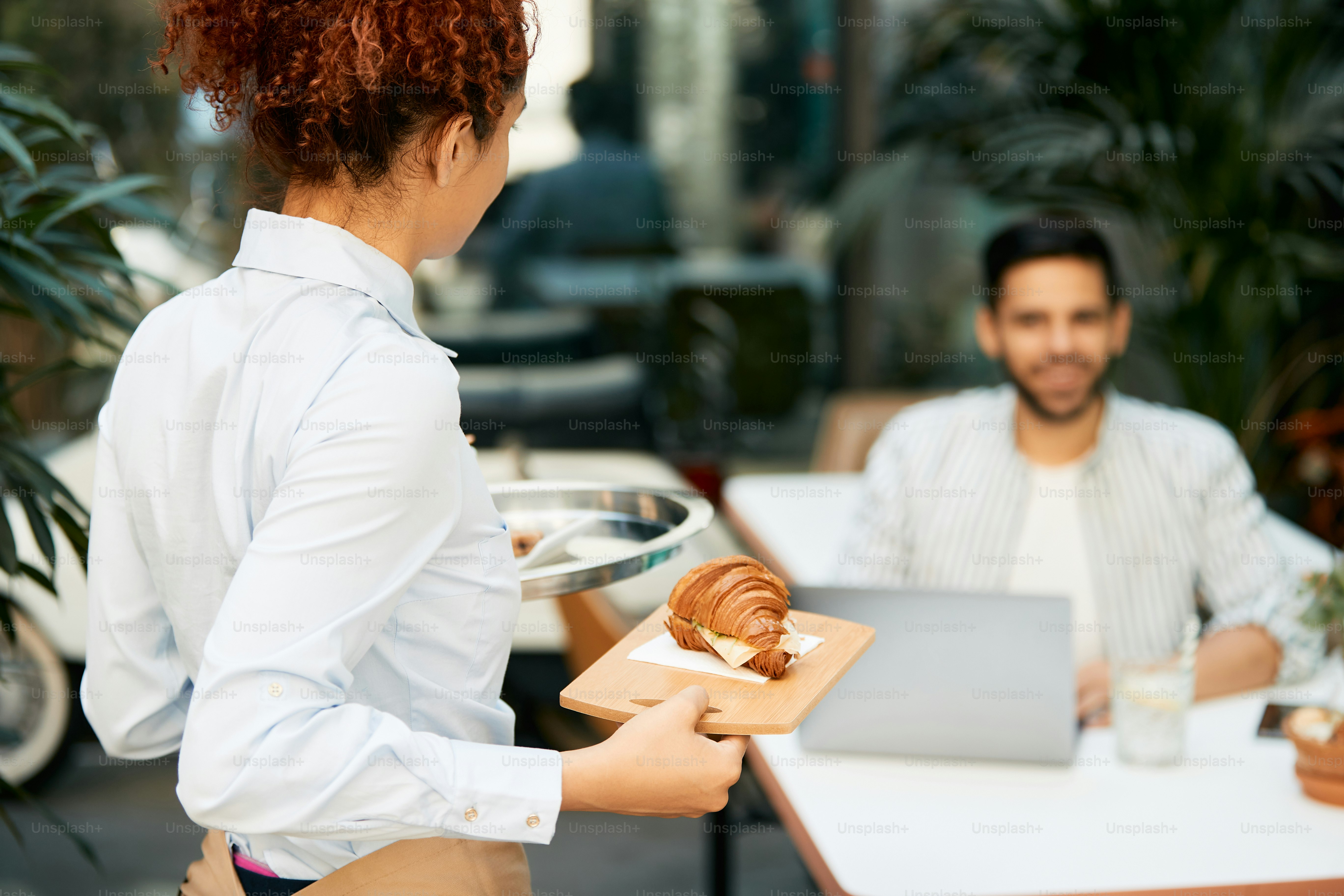 Close-up of waitress serving a customer with croissant in a cafe.