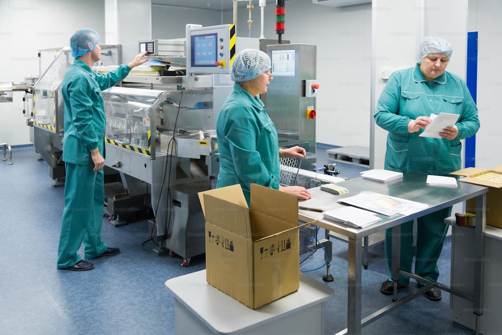 Pharmaceutical technicians work in sterile working conditions at pharmaceutical factory. Scientists wearing protective clothing