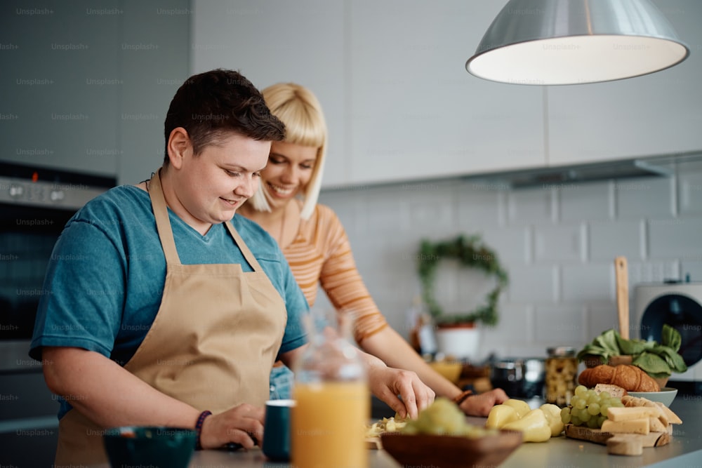 Lächelnde Lesbe genießt es, mit ihrer Freundin in der Küche Essen zuzubereiten.
